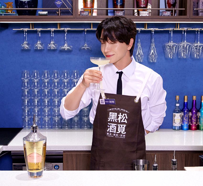 利特身穿工作圍裙於店內陳列區與「創世者」酒款合影展現親切形象。